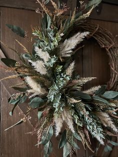 a wreath hanging from the side of a door with dried grass and leaves on it