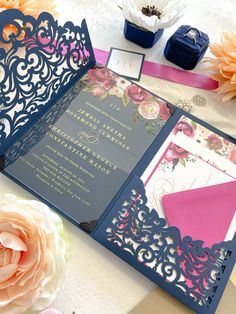 a blue and pink wedding card with flowers on the table next to it is an open pocketfold