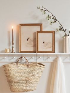 a basket hanging on a wall next to two framed pictures and a candle in a vase