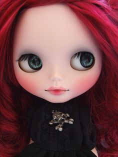 a close up of a doll with red hair and green eyes wearing a black dress