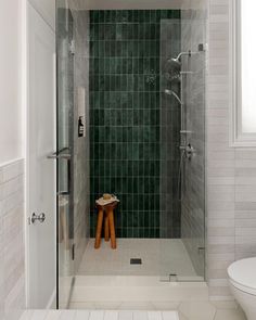 a walk in shower sitting next to a white toilet and sink with green tile on the walls