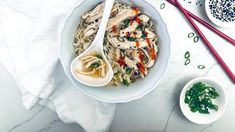 a white bowl filled with noodles and chicken on top of a table next to chopsticks