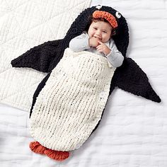 a baby in a penguin costume is laying on a bed with a knitted blanket