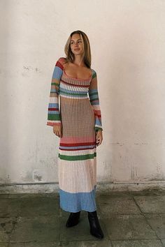 a woman standing in front of a white wall wearing a multicolored sweater dress