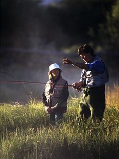 two people standing in the grass with fishing rods