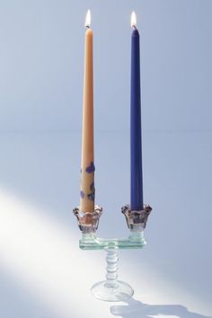 two candles sitting next to each other on top of a glass stand with one candle in the middle