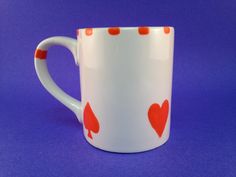 a white coffee mug with red hearts on it sitting on a purple surface in front of a blue background