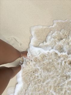 a woman's feet in the sand at the beach with foamy water behind her