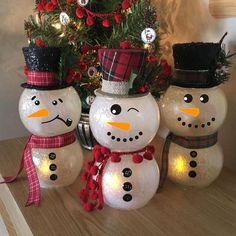 three snowmen sitting next to a christmas tree