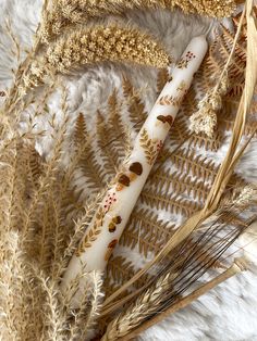 two white candles sitting on top of a fur covered floor next to dry grass and dried plants