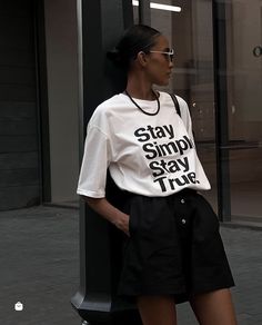 a woman leaning against a pole wearing a white shirt and black shorts with the words stay simple, stay true on it