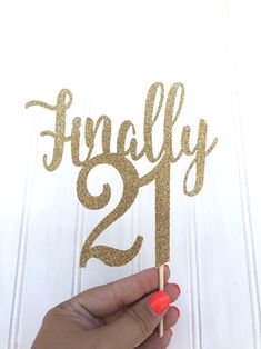 a hand holding a cake topper with the number twenty one on it and gold glitter