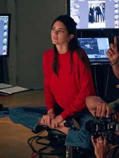 a woman sitting on the floor in front of two monitors and holding a video camera