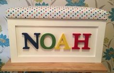 the word noah spelled with colorful letters on a wooden bench in front of a floral wallpaper