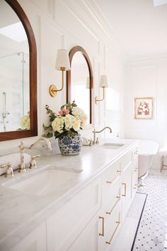 a white bathroom with marble counter tops and double sinks in front of an oval mirror