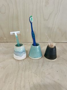 two toothbrushes in cups sitting on a counter next to each other, one blue and the other white