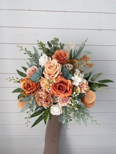 a bridal bouquet with oranges, white and pink flowers in front of a wall