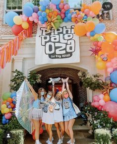 three girls are standing in front of a building with balloons and streamers on it