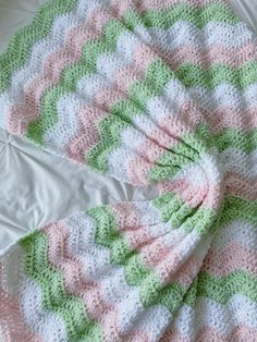 a crocheted blanket laying on top of a bed next to a white pillow