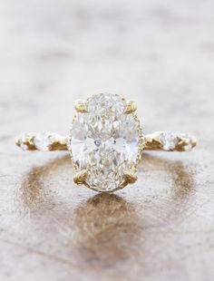 an oval cut diamond ring with three small diamonds on the band, set in 18k yellow gold