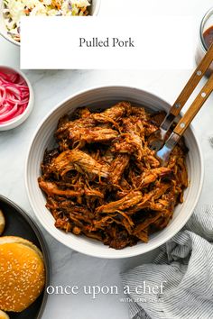 pulled pork in a white bowl with coleslaw and pickles on the side