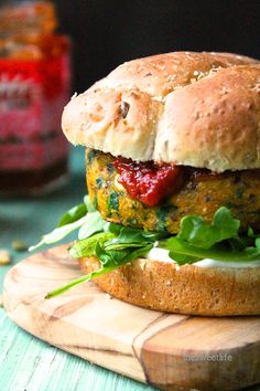 a burger with lettuce and tomato sauce on a cutting board next to a jar of ketchup