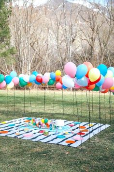 a bunch of balloons are in the air on a picnic table with plates and cups