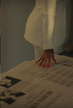 a person's hand on top of a newspaper with red nails and white dress