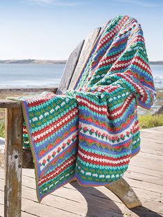 a wooden bench with a blanket draped over it on top of it next to the ocean