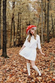 a woman in white dress and red hat walking through leaves