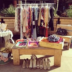 a wooden table topped with lots of clothes and shoes next to a potted plant