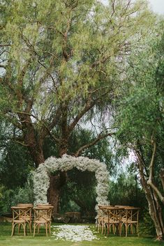 an outdoor ceremony setup with white flowers and greenery on the ground under a large tree