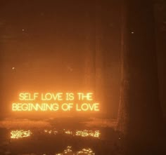 a neon sign that says self love is the beginning of love in front of trees