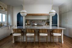 a large kitchen with marble counter tops and wooden chairs around the island in front of two hanging lights