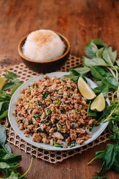 a white plate topped with meat and greens next to a bowl of rice on top of a wooden table