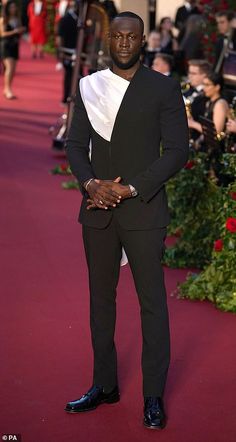 a man in a tuxedo standing on a red carpet with people behind him