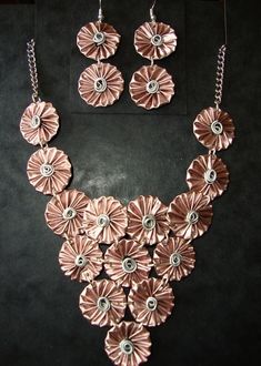 a necklace and earring set made out of pink metal flowers on a black background