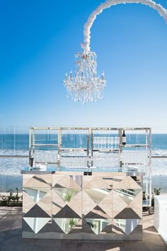 an outdoor bar with a chandelier hanging from it's ceiling next to the ocean