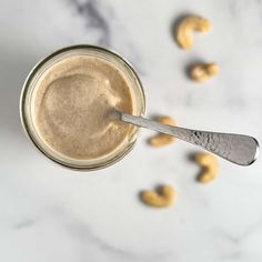 peanut butter in a glass jar with a spoon on the side and cashews scattered around it