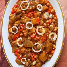 a white plate topped with meat and veggies covered in sauce on top of a pink table cloth