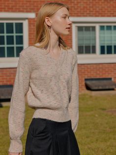 a woman standing in front of a red brick building wearing a sweater and pleated skirt