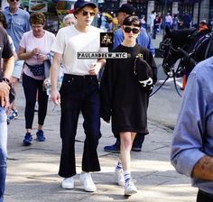 two people walking down the street in front of a group of people wearing hats and sunglasses