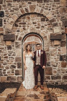 a bride and groom standing on steps in front of an old stone building with arched doorway