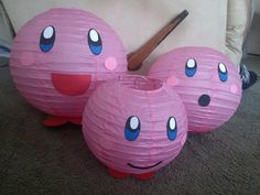 three pink paper lanterns with blue eyes and nose designs on them sitting on the floor