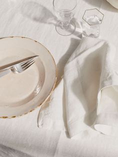 an empty plate and silverware on a white table cloth with napkins, glasses and utensils