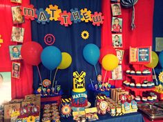 a table topped with balloons and pictures next to a wall covered in red, blue and yellow decorations