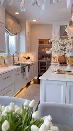 a kitchen filled with lots of white furniture and flowers on top of a wooden table