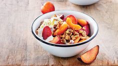 two bowls filled with fruit and granola on top of a wooden table next to sliced peaches