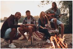 four people sitting around a campfire and smiling at the camera while one plays guitar