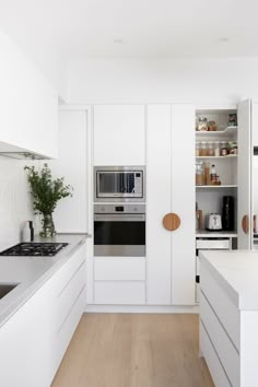 a kitchen with white cabinets and an oven next to a stove top oven on a wooden floor